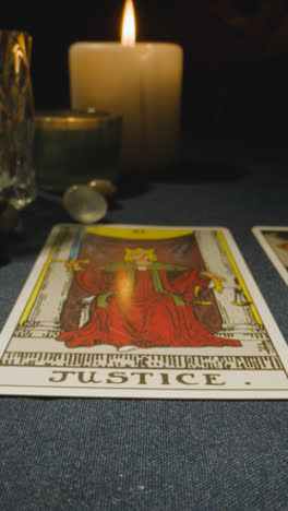 Vertical-Video-Close-Up-Shot-Of-Person-Giving-Tarot-Card-Reading-Laying-Down-The-Justice-Card-On-Table